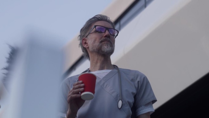 成熟的医生站在医院附近，喝着咖啡聊天