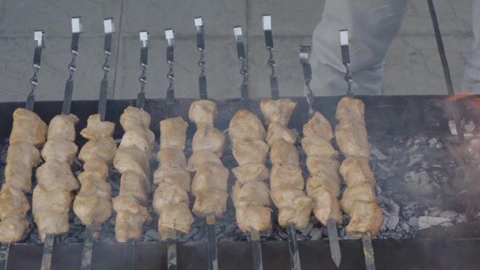鲜嫩多汁的鸡肉串在烤架上烤着。厨师用拨火棍搅煤。美味的烤肉串或羊肉串