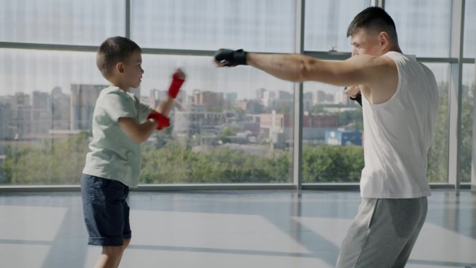 小男孩和成年男子在家庭体育俱乐部练习拳击动作对着窗户背景