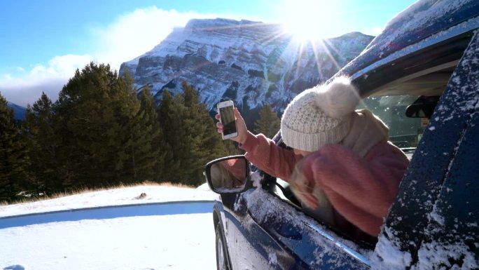 游客在车内用智能手机拍摄雪山，旅游目的地寒假