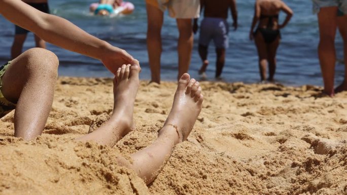 孩子，在沙滩上用羽毛挠兄弟姐妹的脚，孩子盖在沙子里，笑着，笑着，享受着一些乐趣