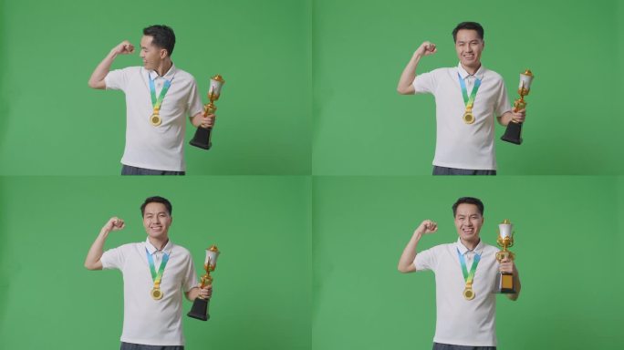 一名亚洲男子拿着金牌和奖杯，在摄影棚的绿幕背景下，对着镜头微笑，展示着他的二头肌