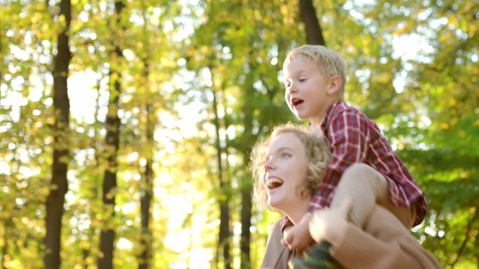 妈妈和儿子在秋天的公园里玩得很开心。一位美丽的妇女把她的小孩抱在肩上。