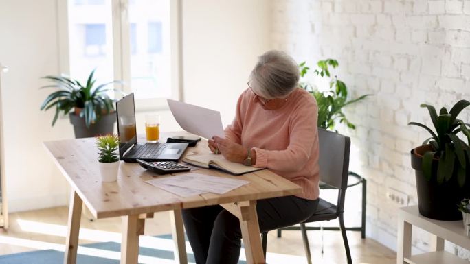 沉思的老妇人在家用笔记本电脑上网付账。资深女商人从事计算机工作。