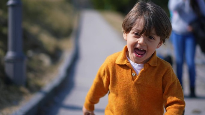 快乐兴奋的小男孩在秋日穿着黄色套头衫跑在外面。孩子的特写脸在运动中向前奔跑，感觉无忧无虑