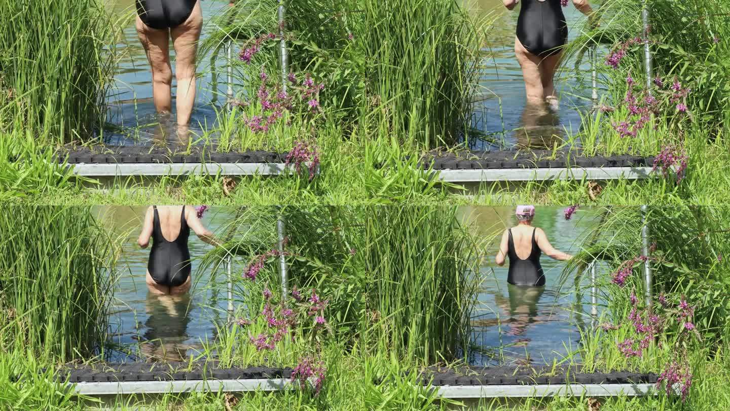 一个长着脂肪团的成年女子，穿着黑色连体泳衣，慢慢地走进清澈透明的湖水中游泳