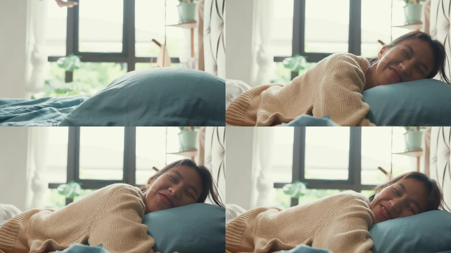 特写亚洲女孩，穿着白色的奶油睡衣，头朝下躺在枕头上，闭上眼睛，开心地微笑，在卧室里柔软的床上感到舒适