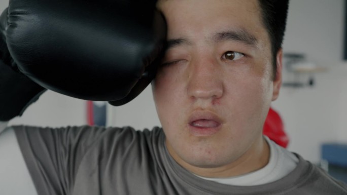 疲惫的亚洲运动员在休息时用拳击手套擦去脸上的汗水的特写