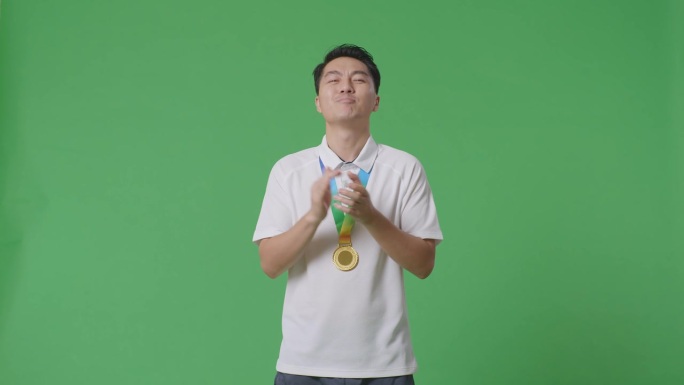 亚洲男子戴着金牌，自豪地鼓掌，成为工作室绿幕背景下的第一位获奖者