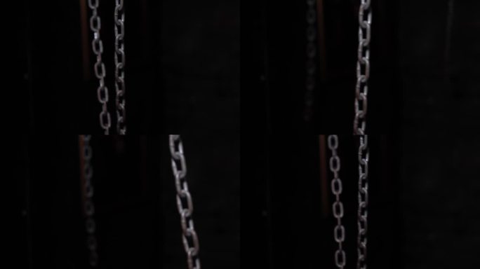 在黑暗的房间里挂着金属链子，铁链左右摆动。