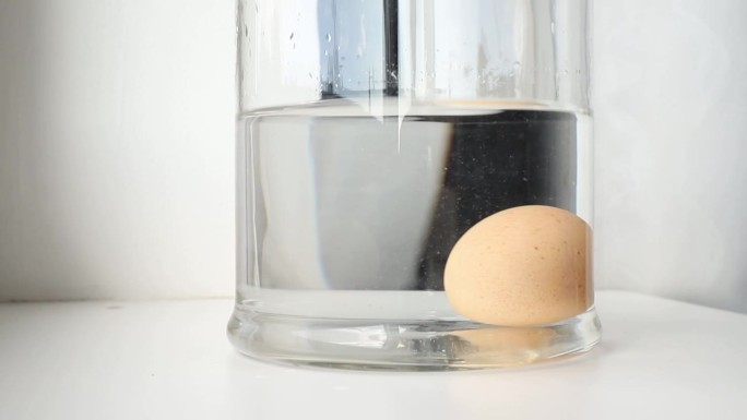比较新鲜可食用和老臭鸡蛋。新鲜的可食用鸡蛋沉在玻璃罐的底部，坏的臭鸡蛋浮在水面上。在家庭厨房里。