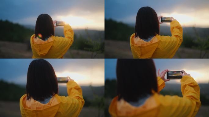 在寒冷多雨的天气里，穿着黄色雨衣的女人在山上欣赏大自然的美丽，用她的手机在大自然中拍照