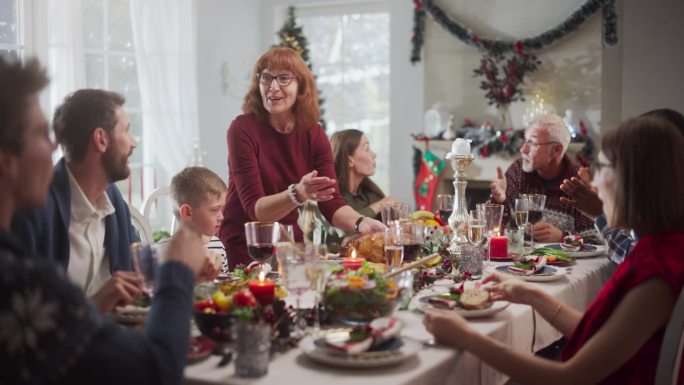 各种各样的年轻人和老人围坐在圣诞餐桌旁，品尝美味的火鸡大餐。当他们在家里一起庆祝时，有趣的谈话和节日