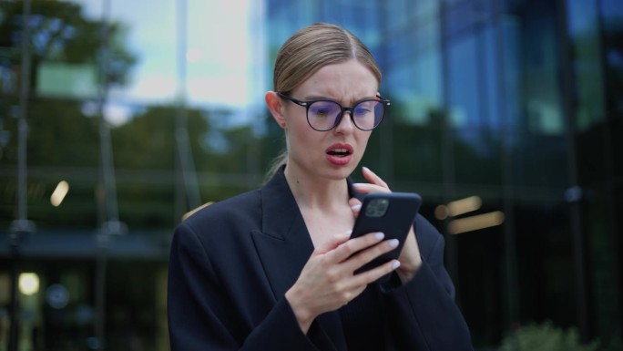 优雅的商务女性站在户外读着智能手机上可怕的消息，因为收到可怕的坏消息而感到不愉快的负面情绪。女女孩在