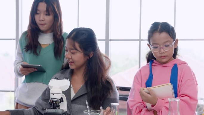 在小学科学课上，小女孩尝试用显微镜观察放在桌子上的微生物，她在做实验笔记。