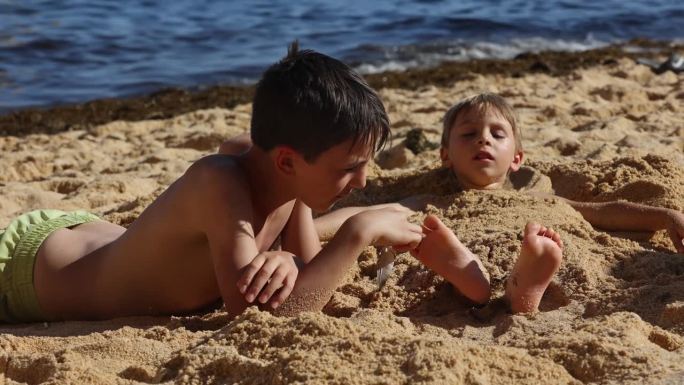 孩子，在沙滩上用羽毛挠兄弟姐妹的脚，孩子盖在沙子里，笑着，笑着，享受着一些乐趣