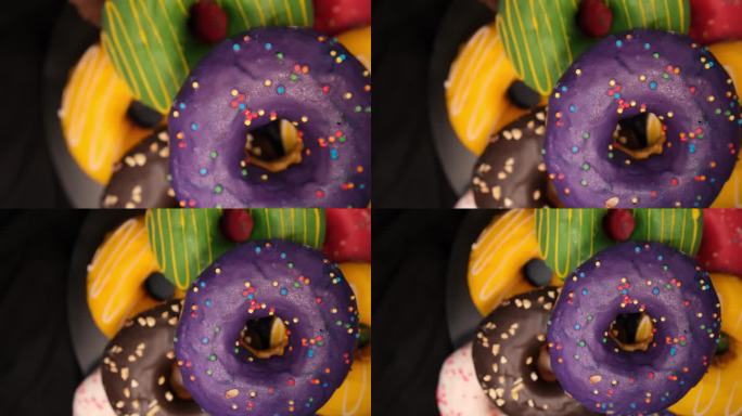 不同颜色的甜甜圈旋转在黑色背景跟踪拍摄顶视图。