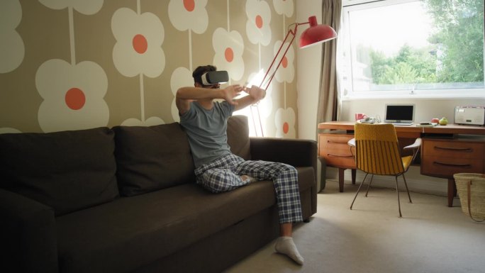 年轻人戴着虚拟现实耳机坐在家里的沙发上观看360度视频想象概念