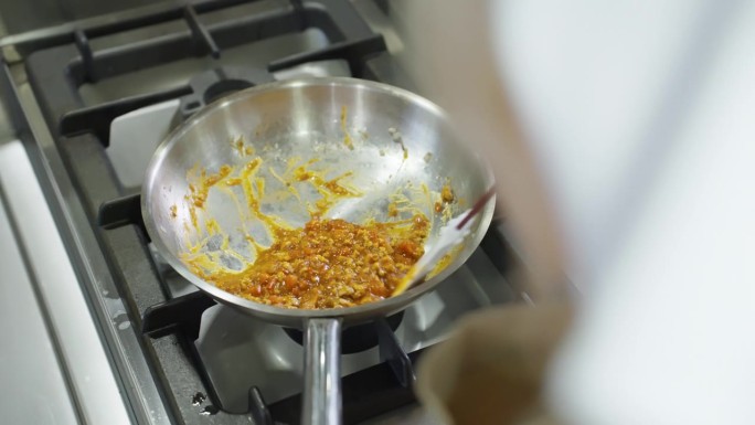 在餐厅的厨房里，妇女用平底锅和铝锅准备黄色食物。技艺高超的女人戴着手套在煤气灶上用平底锅做饭。