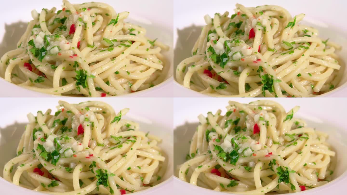白色餐厅盘子里的意大利面淋上奶油酱，自制的意大利面在盘子里旋转，配上大蒜、红辣椒、橄榄油和新鲜欧芹。