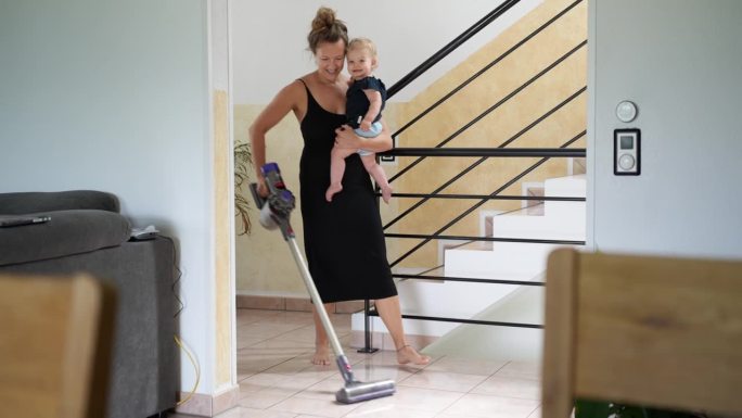 母亲抱着女婴一边打扫房子，一边用吸尘器打扫走廊