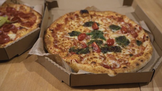整张意大利辣香肠披萨和蔬菜披萨的俯视图，放在桌子上的硬纸板披萨盒里