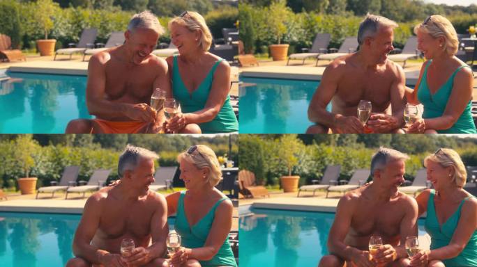 度假的老夫妇坐在躺椅上，在酒店游泳池边用香槟烤面包