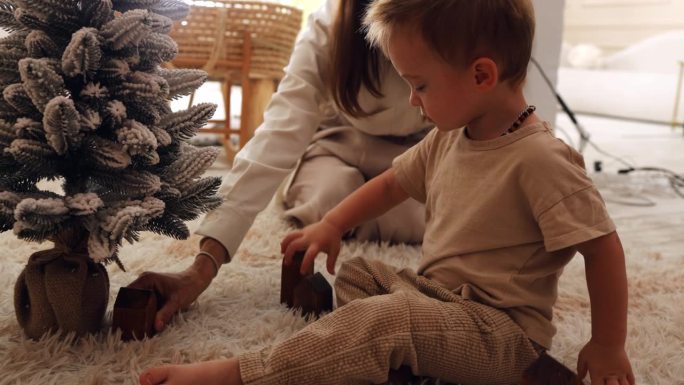 妈妈和她的小儿子在家里木马旁边的一棵小人造圣诞树旁玩耍。孩子在圣诞树旁玩木制玩具