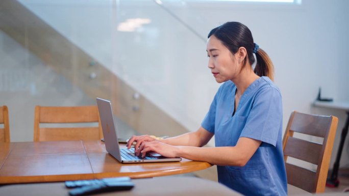 年轻的亚洲医疗保健专业人员穿着手术服在家里开会时用笔记本电脑聊天