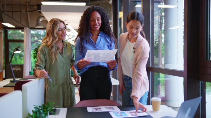 多元文化的女性商业团队在现代办公室的办公桌前开会，审查校样或版面——慢镜头
