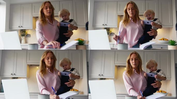 忙碌的工作母亲带着年幼的儿子在厨房用笔记本电脑，而儿子在玩她的手机