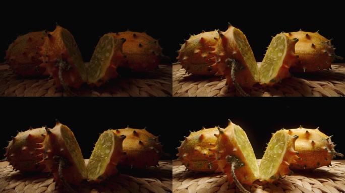 桌子上放着三根长着尖刺的Kiwano橙黄瓜，周围有不同的圆形照明。其中一个被切成薄片。