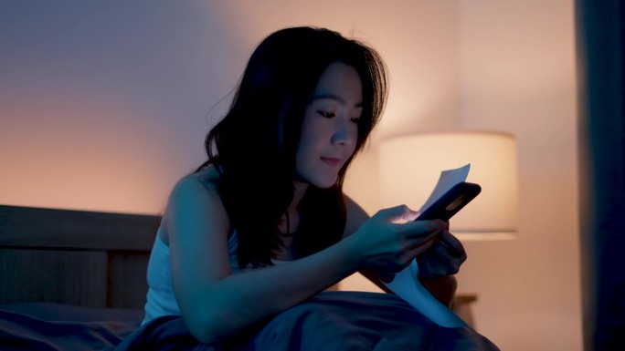 亚洲女性用智能手机扫描二维码支付账单，轻松在家在线支付。