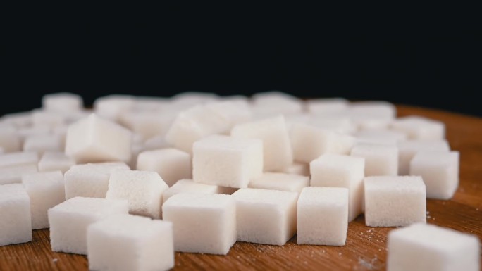 在旋转的木制背景上，白糖块落在一堆糖里