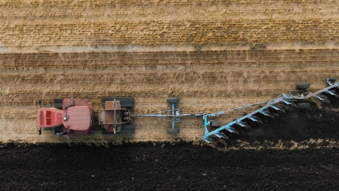 红色的大拖拉机开在橡胶履带上，在田地里拉着多产的反耕犁。为种植新作物准备土壤，农业。拖拉机田间耕作的