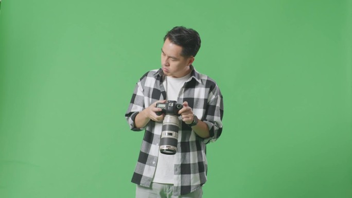 亚洲摄影师站在摄影棚的绿幕背景上，看着相机里的照片，然后头痛