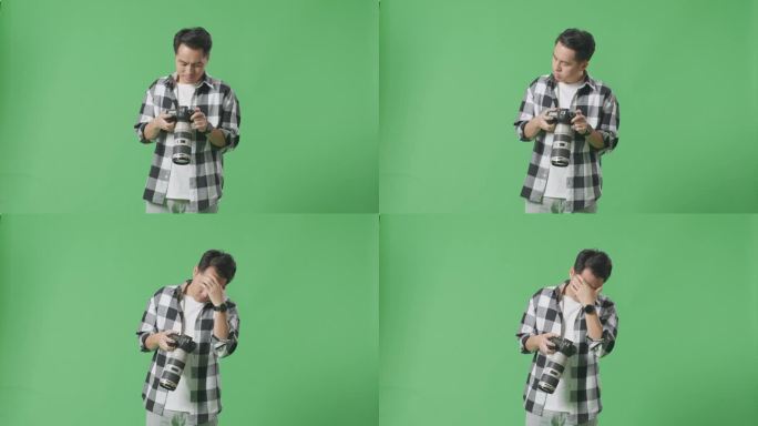 亚洲摄影师站在摄影棚的绿幕背景上，看着相机里的照片，然后头痛