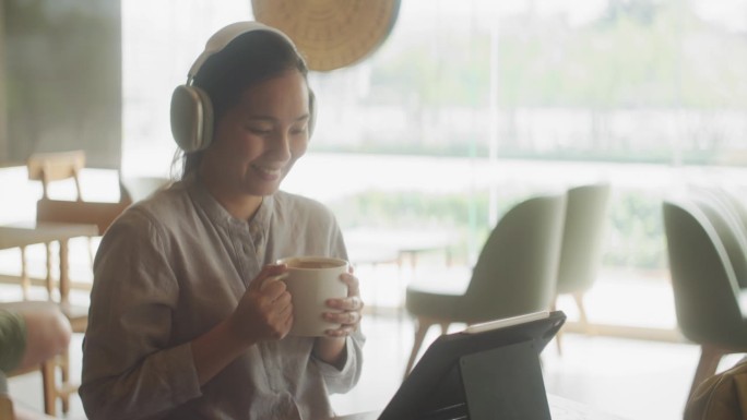 快乐的亚洲女人在咖啡店看着笔记本电脑