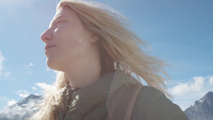 在山顶上的女人的特写肖像，金色的头发在风中吹过云层，在挪威慢动作观看徒步旅行者女孩