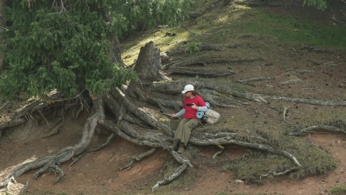 女游客在山林徒步时坐在树根上打电话