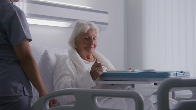 老妇人在明亮的病房里吃着美味的食物