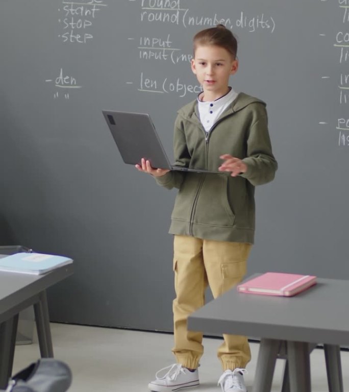 小男孩在教室里拿着笔记本电脑做报告