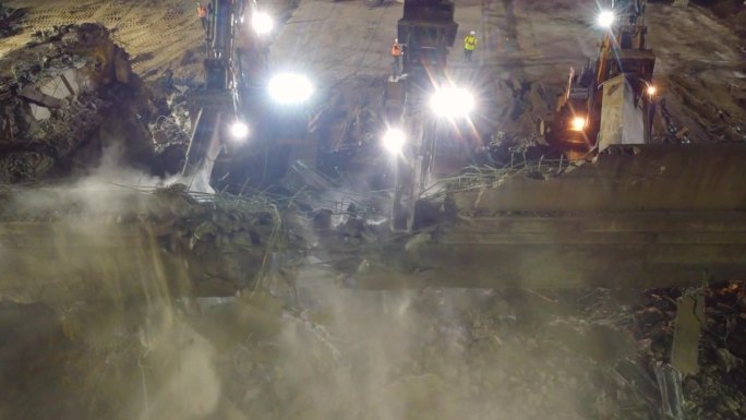 多个工作人员在夜间使用液压钳挖掘机拆除一座旧建筑