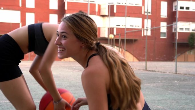 这个长头发的金发女孩和她的中国朋友在夏天打篮球前在地板上大笑。