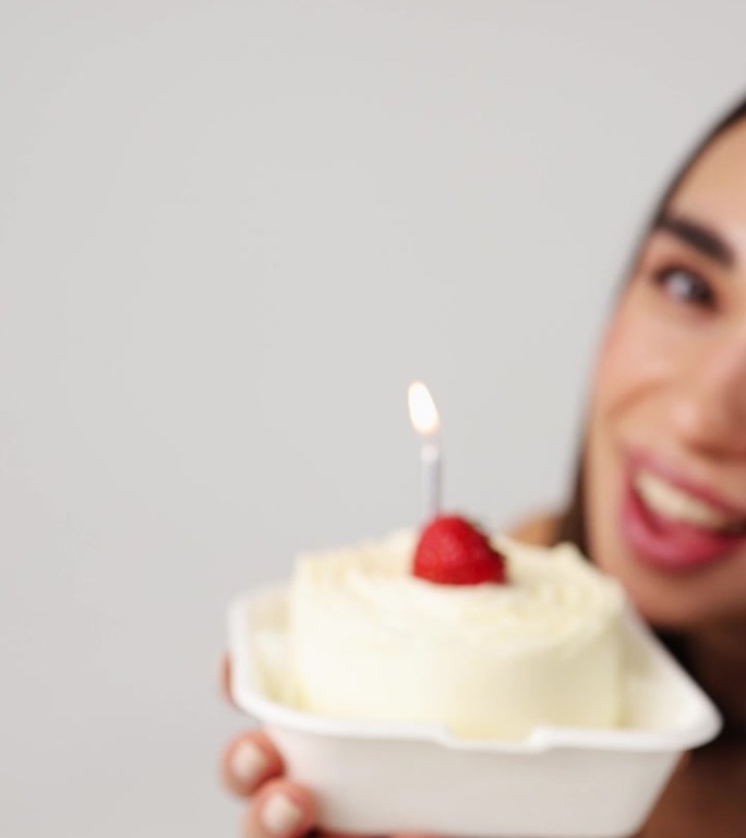 有草莓和蜡烛的蛋糕特写。这个女孩手里拿着一个白色背景的节日蛋糕。垂直视频。生日庆祝活动