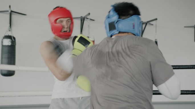 职业拳击手在体育中心的拳击场上训练，年轻人戴着防护头盔和手套出拳