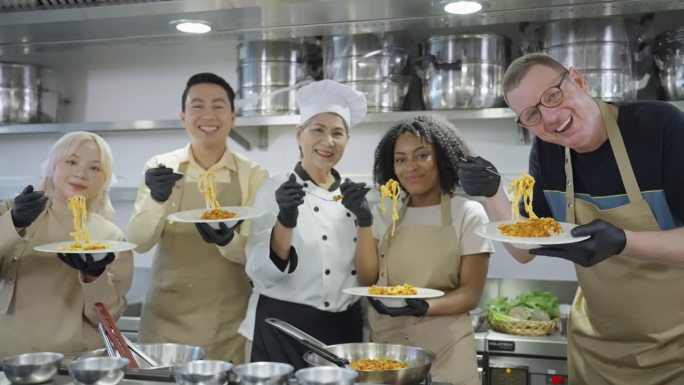 一群非常专业的烹饪学生和专业的亚洲厨师穿着白色的烹饪服和她的学生戴着围裙展示白色的意大利面或用新鲜食