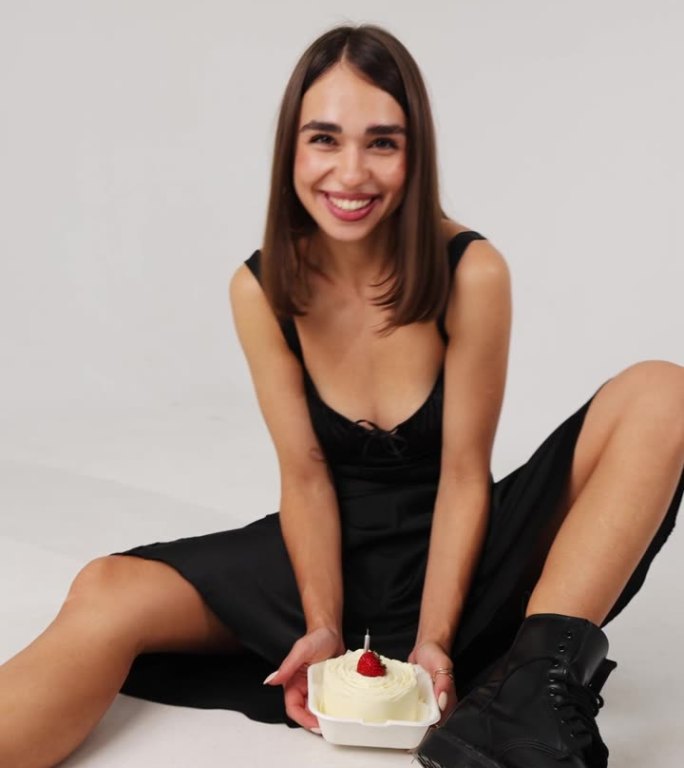 哥特女孩非正式地庆祝她的生日。垂直视频。一个穿着短裙和黑丝袜的女孩拿着蜡烛和草莓吃着节日蛋糕。两腿之