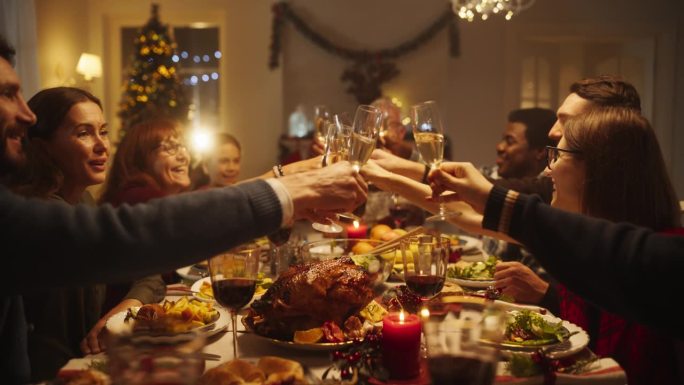 家人、孩子和朋友在下午一起在家吃圣诞晚餐。多元文化家庭抚养孩子，碰杯香槟，用美味的火鸡大餐庆祝节日