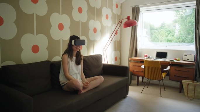 年轻女子戴着虚拟现实耳机坐在家里的沙发上观看360度视频想象概念
